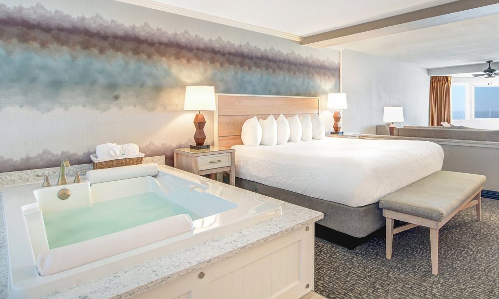 Hotel room featuring a jetted tub beside the bed, modern furnishings, soft lighting, and coastal style
